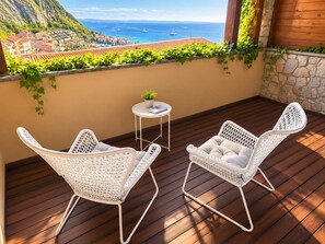 A balcony with two white wicker chairs, a small round table, and a potted plant. - Profumo di mare - Portopiccolo Apartments (Sistiana)