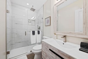 Un baño moderno con ducha envuelta en vidrio, inodoro blanco y tocador con lavamanos y espejo.