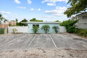A parking lot with a light blue building, palm trees, and a gated entrance. - NEW LISTING: Charming 2-Bedroom Deerfield Beach Apartment Near Beach & Shops (Deerfield Beach)