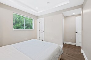 A bedroom with a bed, a window with blinds, and two doors leading to other rooms. - NEW LISTING: Charming 2-Bedroom Deerfield Beach Apartment Near Beach & Shops (Deerfield Beach)
