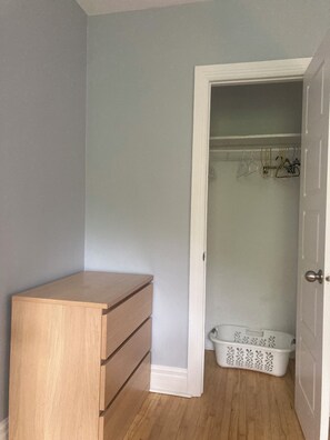 A room with a wooden dresser, a white door leading to a closet, and a white laundry basket. - Quiet apartment near Molson Park: two bedrooms, living room, full kitchen (Montréal)