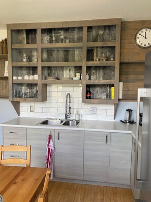 Eine Küche mit integriertem Spülbecken, Holzregalen und einer Uhr an der Wand.
