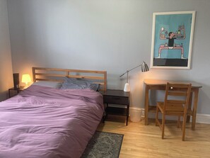 A bedroom with a bed, bedside table, lamp, desk, chair, and a painting on the wall. - Quiet apartment near Molson Park: two bedrooms, living room, full kitchen (Montréal)