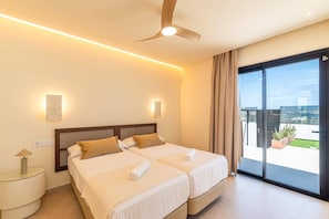 A hotel room with two beds, a ceiling fan, a large window with a view, and a small bedside table with a lamp. - Villa Fragata by Villa Plus (Corralejo)