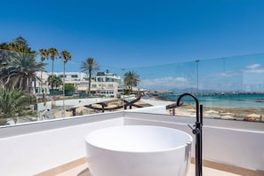 A balcony with a white bathtub, overlooking a beach with palm trees and a clear sky. - Villa Fragata by Villa Plus (Corralejo)