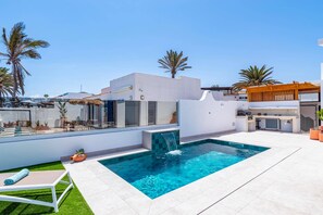 Uma área moderna com piscina ao ar livre, piscina azul cristalina, espreguiçadeira e espaço para churrasco.
