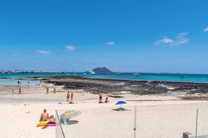 A beach with people sunbathing, a boat, and a mountain in the background. - Villa Fragata by Villa Plus (Corralejo)