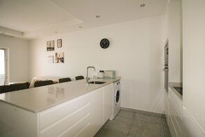A modern kitchen with a central island, a built-in washing machine, and a clock on the wall. - FLH Vale do Lobo Delightful Terrace (Vale do Lobo)