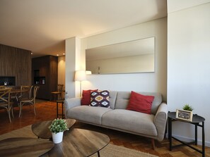 A modern living room with a sofa, coffee table, and a dining area with chairs and a table. - FLH Boavista: Stylish Apartment with a View (Porto)