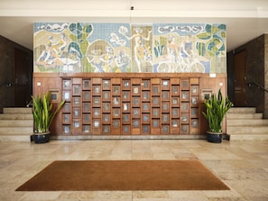A lobby with a tiled wall mural, a wooden reception desk with numbered slots, and potted plants. - FLH Boavista: Stylish Apartment with a View (Porto)