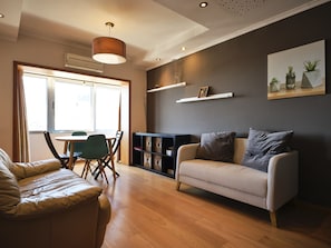 A modern living room with a sofa, a dining table with chairs, a bookshelf, and a large window. - FLH Porto Central Comfy Duplex (Porto)