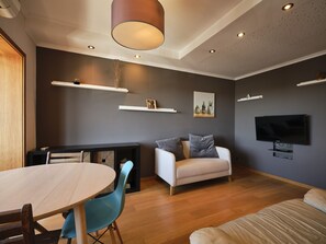 Un salon moderne avec un téléviseur à écran plat, un canapé, une table à manger avec des chaises et un plancher en bois.