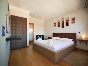 Une chambre d’hôtel avec un lit en bois, une table de chevet, une lampe fixée au mur et des œuvres d’art.