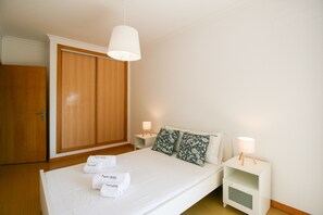 A bedroom with a bed, two bedside tables with lamps, a wardrobe, and two towels on the bed. - FLH Olhão Minimalist Apartment with Balcony (Olhão)