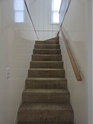 A carpeted staircase with a wooden handrail, leading to a landing with a window. - Cozy Allen Park Bungalow (Allen Park)