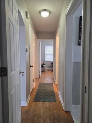 A hallway with wooden flooring, white doors, and a ceiling light fixture. - Cozy Allen Park Bungalow (Allen Park)