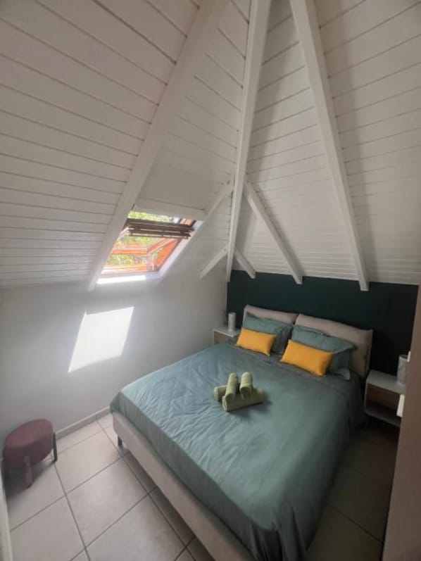 A bedroom with a sloped ceiling, a bed with a blue bedspread, and a window providing natural light.