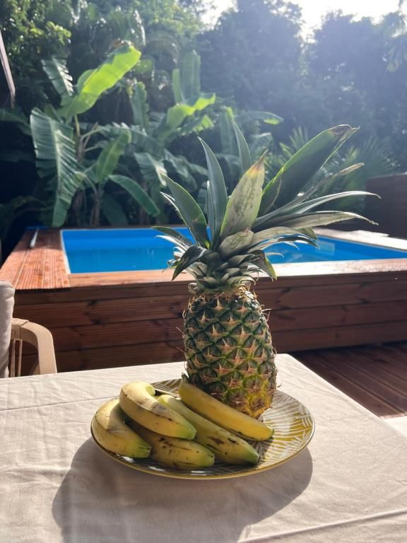 Una mesa con un plato de plátanos y una piña, una terraza de madera y una piscina al fondo.