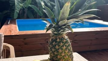Ett bord med en tallrik full av bananer och en ananas, ett trädäck och en pool i bakgrunden.