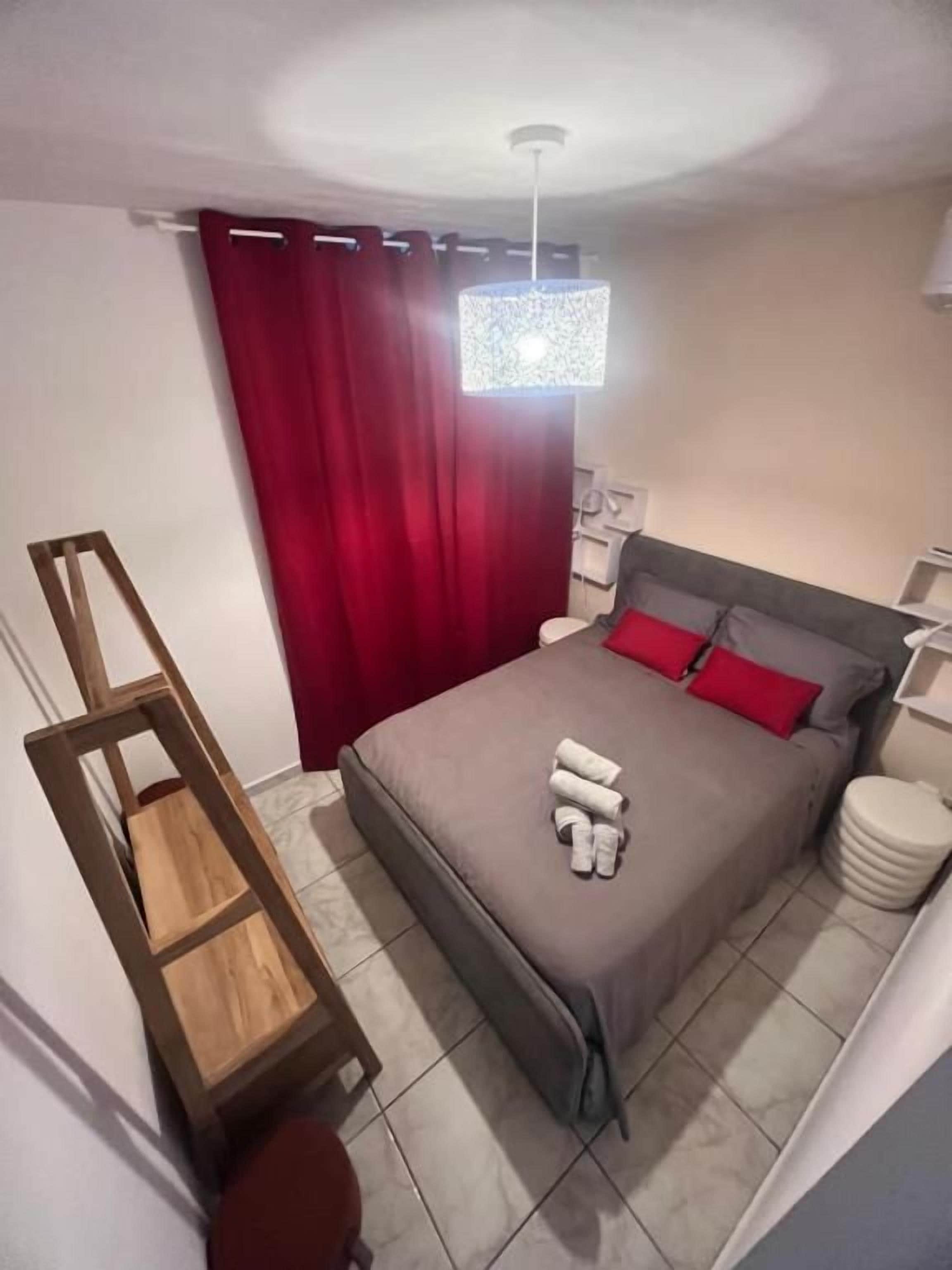 A bedroom with a bed, a wooden ladder, a red curtain, a white bedside table, and a white lamp.