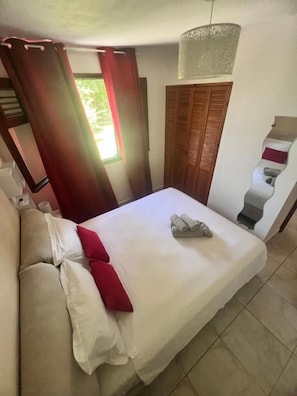 Habitación de hotel con cama, sofá, ventana con cortinas, puerta de madera y lámpara fijada a la pared.