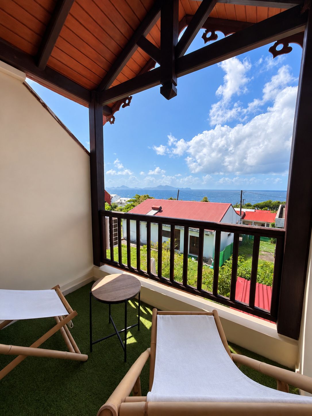 Un balcon avec vue sur les maisons et la mer, équipé d’une table et de deux chaises.