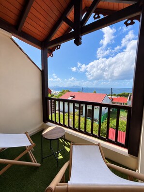 Un balcón con vistas a casas y al mar, equipado con una mesa y dos sillas.