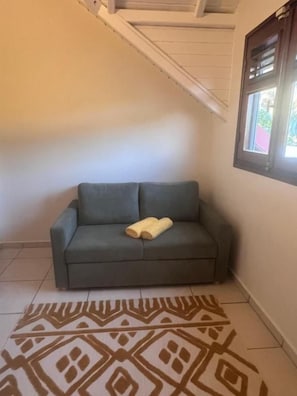 Un sofá gris con una toalla amarilla, una alfombra estampada y una ventana con persianas.