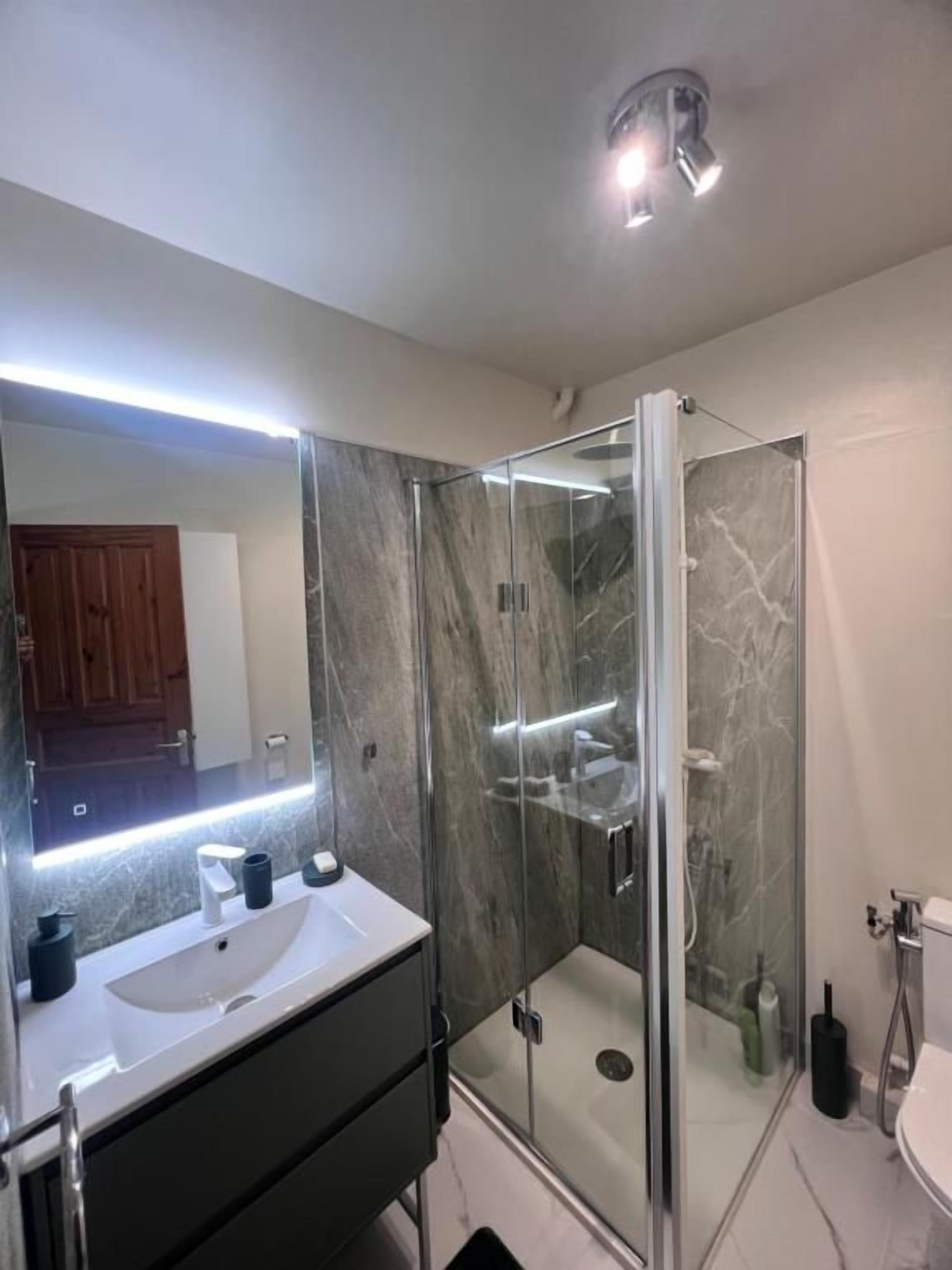 Une salle de bain moderne avec une douche à parois de verre, un meuble-lavabo avec un miroir et des toilettes.