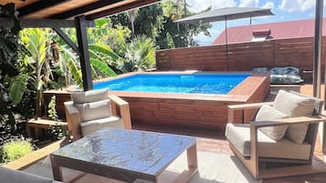 A covered outdoor area with a pool, lounge chairs, and a hot tub.