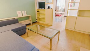 A modern living room with a glass-top coffee table, a grey sofa, and a dining area in the background. - Veronetta Living - Two Bedroom Apartment, Sleeps 5 (Verona)