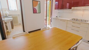 A dining area with a wooden table and chairs, a white sink, and a kitchen with white cabinets and a red appliance. - Veronetta Living - Two Bedroom Apartment, Sleeps 5 (Verona)