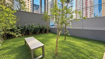 A grassy outdoor area with a wooden bench, a small tree, and a chain-link fence.