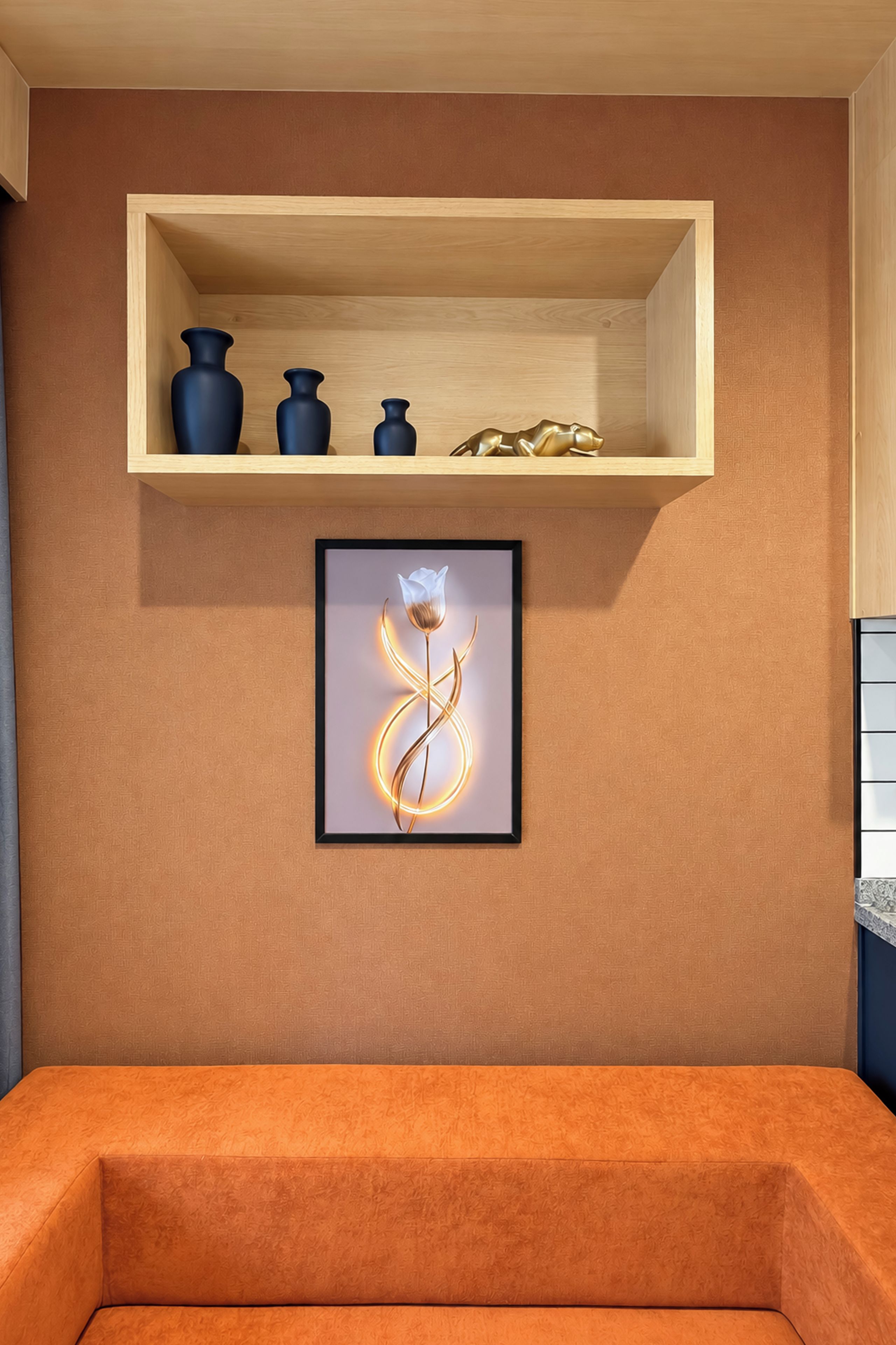 A room with a wooden shelf holding decorative vases, a framed artwork of a flower, and a sofa.