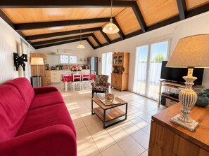 A spacious living area with a red sofa, a coffee table, and a television. - Comfortable chalet 150m from Grève Blanche beach (Plouguerneau)