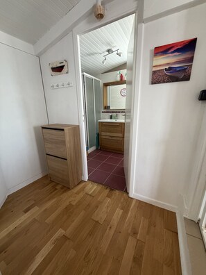 A room with a wooden floor, a wooden cabinet, a bathroom with a mirror, and a painting on the wall. - Comfortable chalet 150m from Grève Blanche beach (Plouguerneau)
