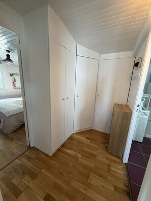 A room with a wooden floor, white wardrobe, and a small wooden cabinet. - Comfortable chalet 150m from Grève Blanche beach (Plouguerneau)