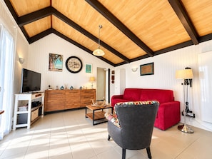 Una sala de estar con un sofá rojo, una televisión, un aparador de madera y un techo con vigas a la vista.