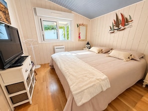 A bedroom with a bed, a television, a window, and a wall decoration. - Comfortable chalet 150m from Grève Blanche beach (Plouguerneau)
