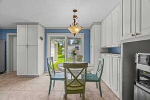 A kitchen with white cabinets, a dining table with chairs, and a hanging light fixture. - Fishermans Retreat - Unit 1 + 2 (entire property) (Satsuma)