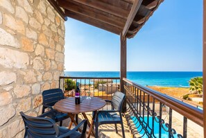 A balcony with a stone wall, a wooden table with chairs, a bottle of wine, and a view of the sea. - Villa Petroktisto - Three Bedroom Villa, Sleeps 6 (Pomos)