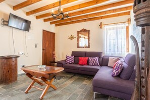 Ein Wohnzimmer mit Holzboden, einer Couch mit Kissen, einem Couchtisch aus Holz und einem an der Wand befestigten Fernseher.