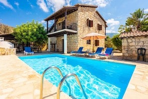 Une villa en pierre dotée d’une piscine, de chaises longues et d’un patio couvert.