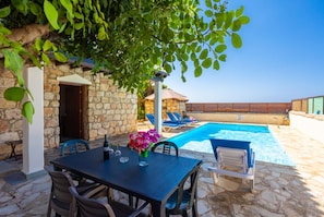 Eine Steinterrasse mit Pool, Sitzgelegenheiten im Freien und einem Tisch mit Getränken.