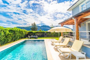 A swimming pool with lounge chairs and umbrellas, surrounded by a hedge and a view of mountains. - Villa Dogakent 4 - Four Bedroom Villa, Sleeps 8 (Okçular)