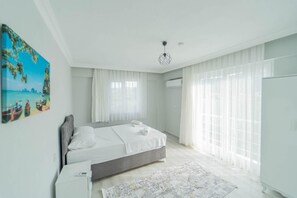 A modern bedroom with a bed, a bedside table, a desk, a chair, a window with sheer curtains, and a wall-mounted air conditioner. - Villa Dogakent 1 - Four Bedroom Villa, Sleeps 8 (Okçular)
