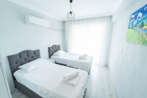 Ein modernes Hotelzimmer mit zwei Betten, einem großen Fenster mit durchsichtigen Vorhängen und einem Bild an der Wand.