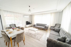 A spacious living room with a dining area, grey upholstered sofas, a flat-screen TV, and a modern chandelier. - Villa Dogakent 1 - Four Bedroom Villa, Sleeps 8 (Okçular)