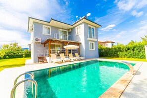 Ein zweistöckiges Haus mit Swimmingpool, einer überdachten Terrasse mit Liegestühlen und einer Satellitenschüssel auf dem Dach.