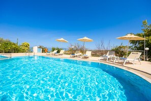 Piscina com água azul cristalina, rodeada por espreguiçadeiras e guarda-sóis, sob um céu límpido.